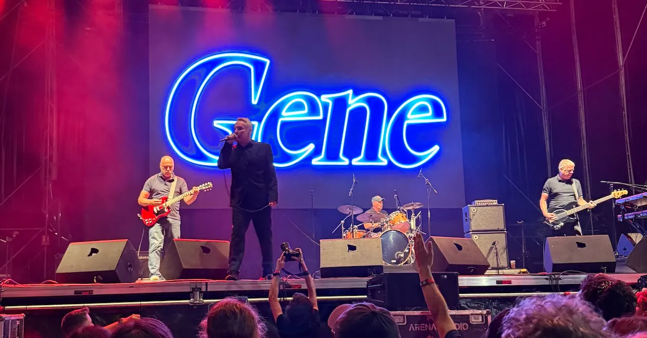 Four musicians on stage with ‘Gene’ in neon above them