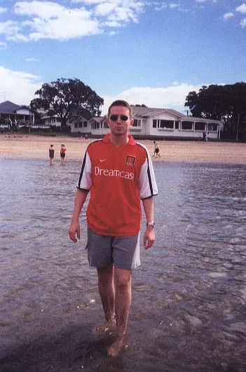 Man paddling on a beach wearing a red Arsenal shirt.