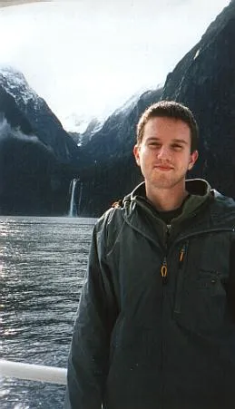 Man in grey anorak standing in front of a sound/fjord