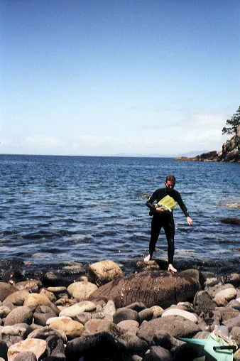 Man holding flippers and walking on rocks on the shore.