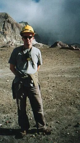 Man in hard hat standing in front of steam at foot of a volcano.